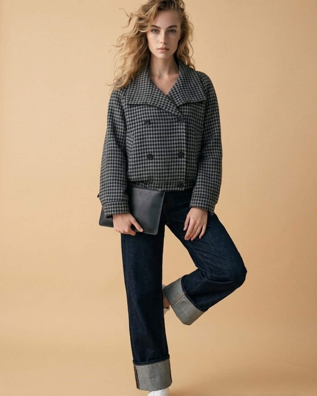 Grey Houndstooth Wool Coat A woman modeling a cropped black and white houndstooth double-breasted jacket, paired with dark blue jeans featuring gray cuffed hems, against a solid beige studio background.