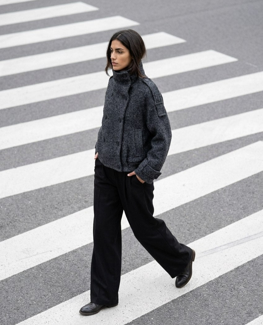 Grey Bouclé Wool Coat A woman walking across a striped crosswalk wearing a dark gray textured cropped jacket, black wide-leg trousers, and black shoes.