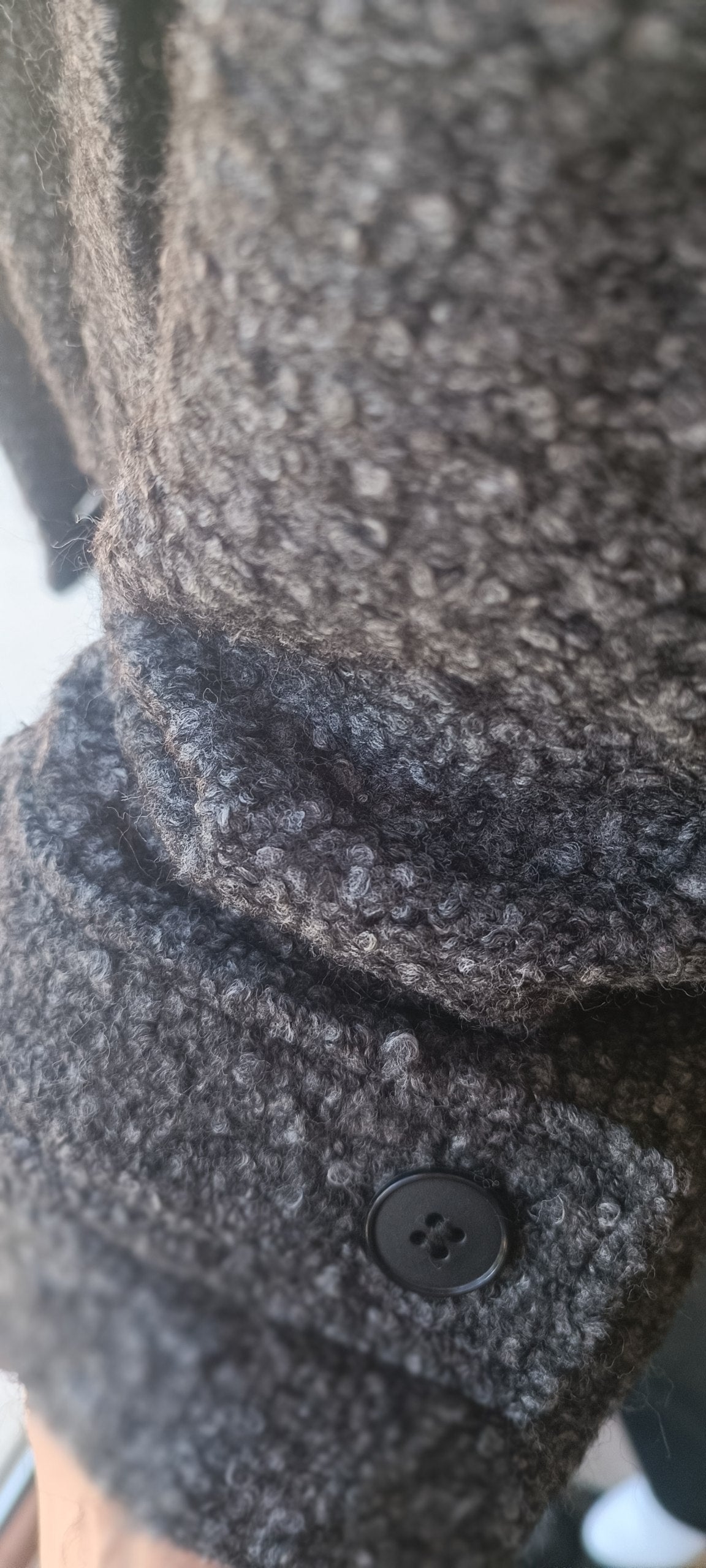 Close-up of a dark gray and black textured knit fabric with a black button detail.