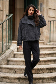 A woman wearing a dark gray textured cropped jacket and black trousers walks down stone steps outdoors.