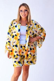 A woman modeling a matching two-piece lounge set featuring a yellow, orange, and navy floral kimono jacket and shorts over a light blue top, set against a plain white studio background.