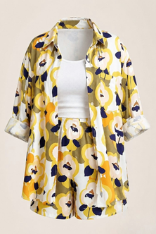 A women's two-piece matching set featuring a short-sleeve button-up shirt and shorts in a bold yellow, navy blue, and white floral pattern, styled over a white ribbed tank top on a mannequin against a solid beige background.
